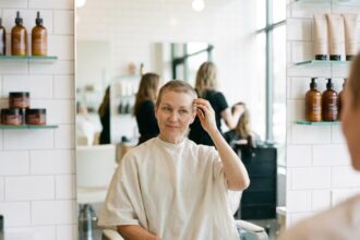 Femme aux cheveux courts en repousse après chimiothérapie assise dans un fauteuil de salon de coiffure, regardant son reflet dans le miroir