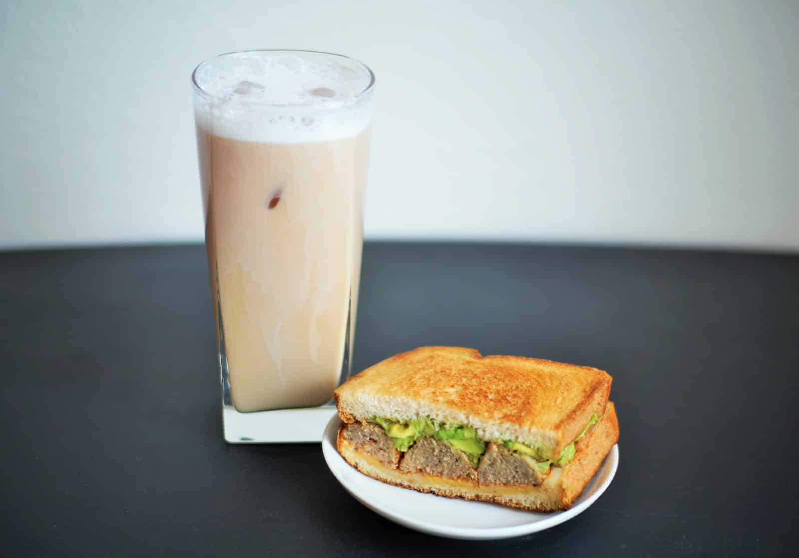 filled drinking glass beside a sliced sandwich